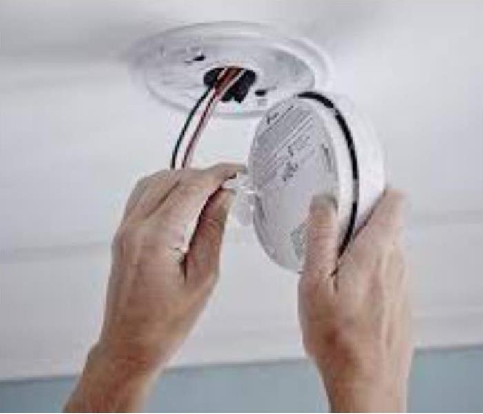 A person installing a smoke detector on a ceiling